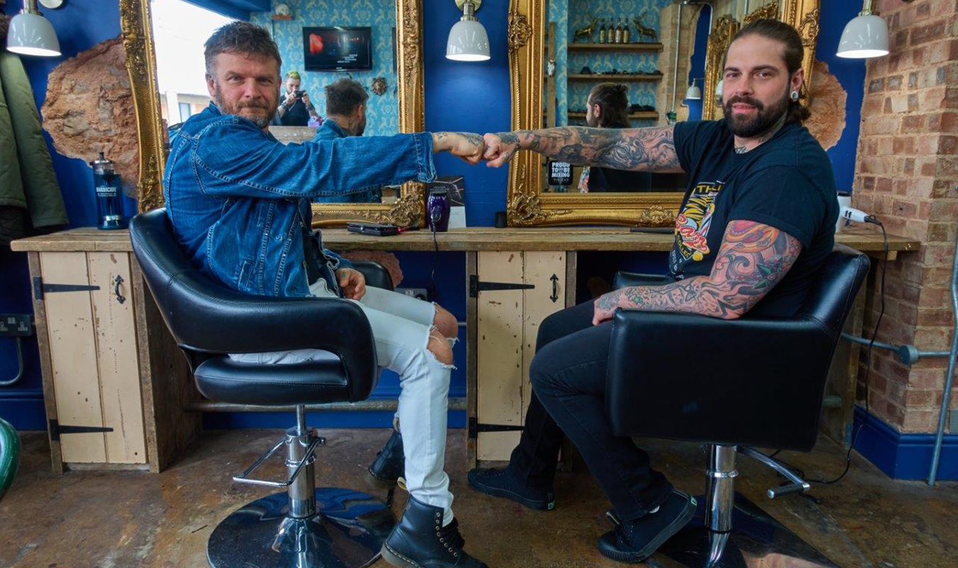 Matthew Pritchard and a barber sitting in barbers chairs, fistbumping