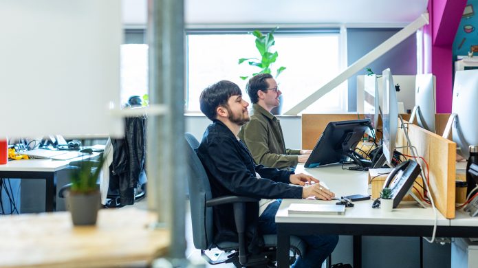 Two members of team Orchard working collaboratively on an integrated marketing agency project while at their desks.