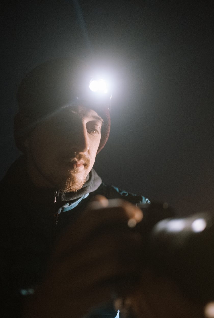 Alyn Wallace an astral photographer looking at his camera at night with only a head torch for light. 